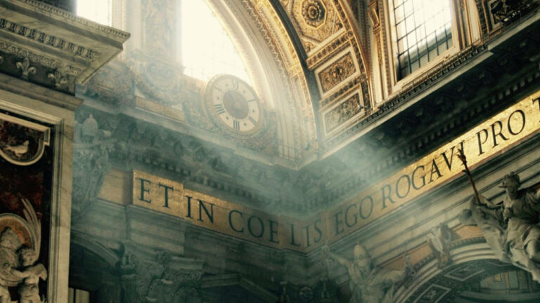 Alcuni raggi di sole entrano dalle vetrate della Basilica di San Pietro, in Vaticano, illuminandone l'interno e una parete con una frase in Latino.