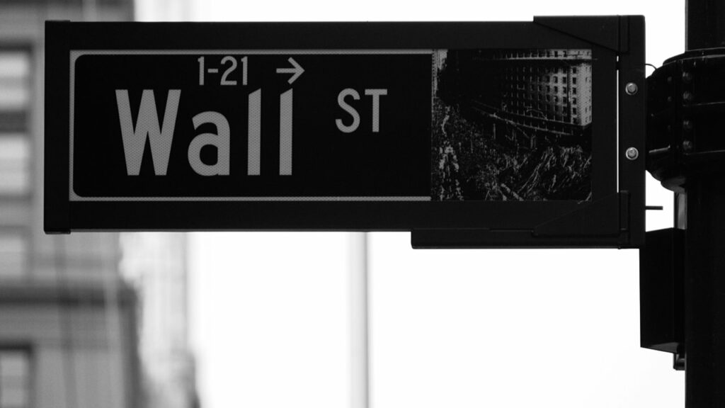 Foto in scala di grigi di un segnale stradale che indica Wall Street, a New York